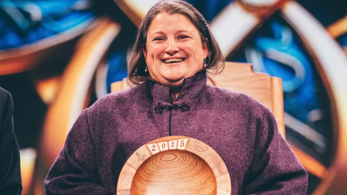 Lucy Cowley yn derbyn ei gwobr ar lwyfan yr eisteddfod. Mae hi'n gwisgo siaced borffor ac mae'r wobr yn fowlen bren gyda '2025' wedi ysgrifennu arni.