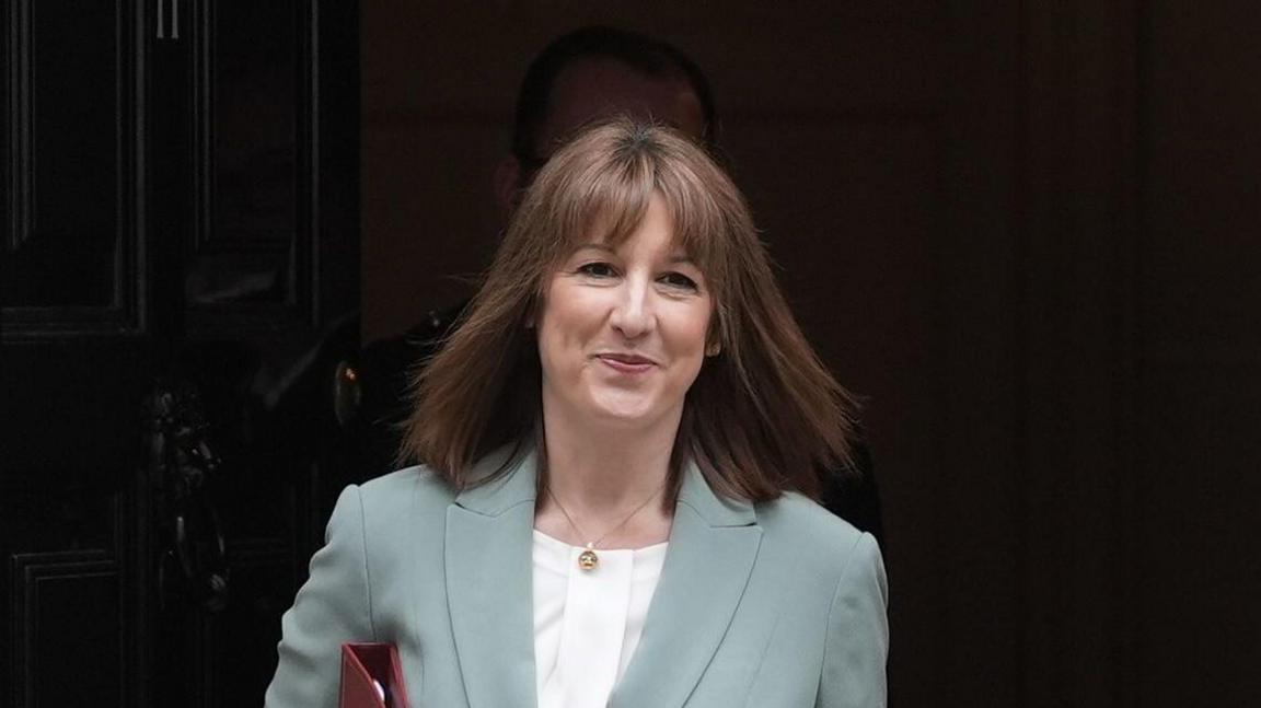Chancellor of the Exchequer Rachel Reeves leaves 11 Downing Street, London, ahead of delivering her spending review in the House of Commons. She has shoulder length brown hair and wears a pale green suit jacket with a white blouse underneath.