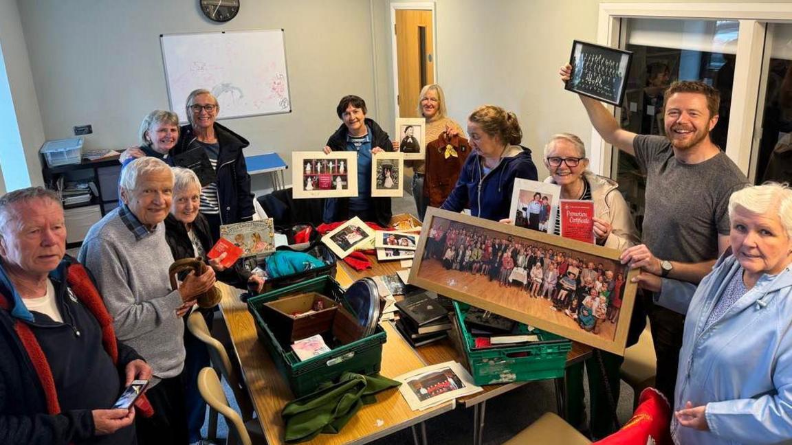 Parishioners are gathered round a table which has boxes of photographs on top of it celebrating the retrieval of the photos from the fire.