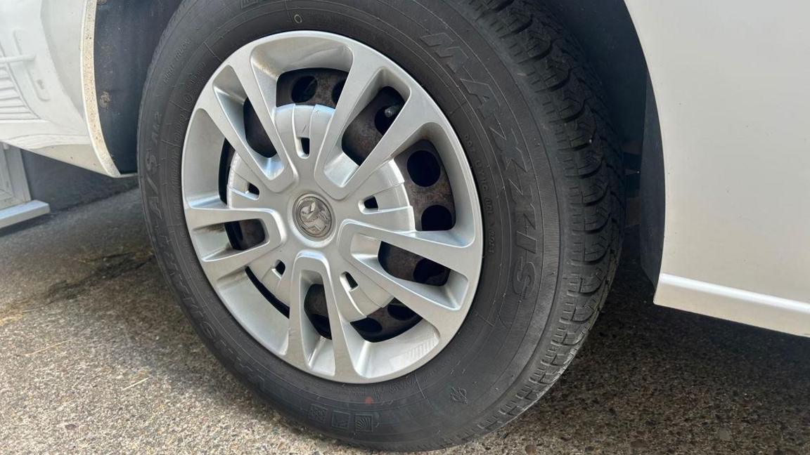 A close up of a car wheel on a white car. The tyre is black with a silver hubcap.