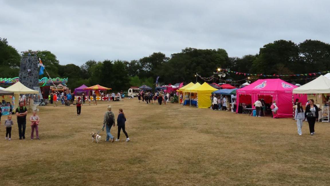 People walk around Saumarez Park in Guernsey during the North Show. Several small marquees are up along the edge of the field along with fairground rides.