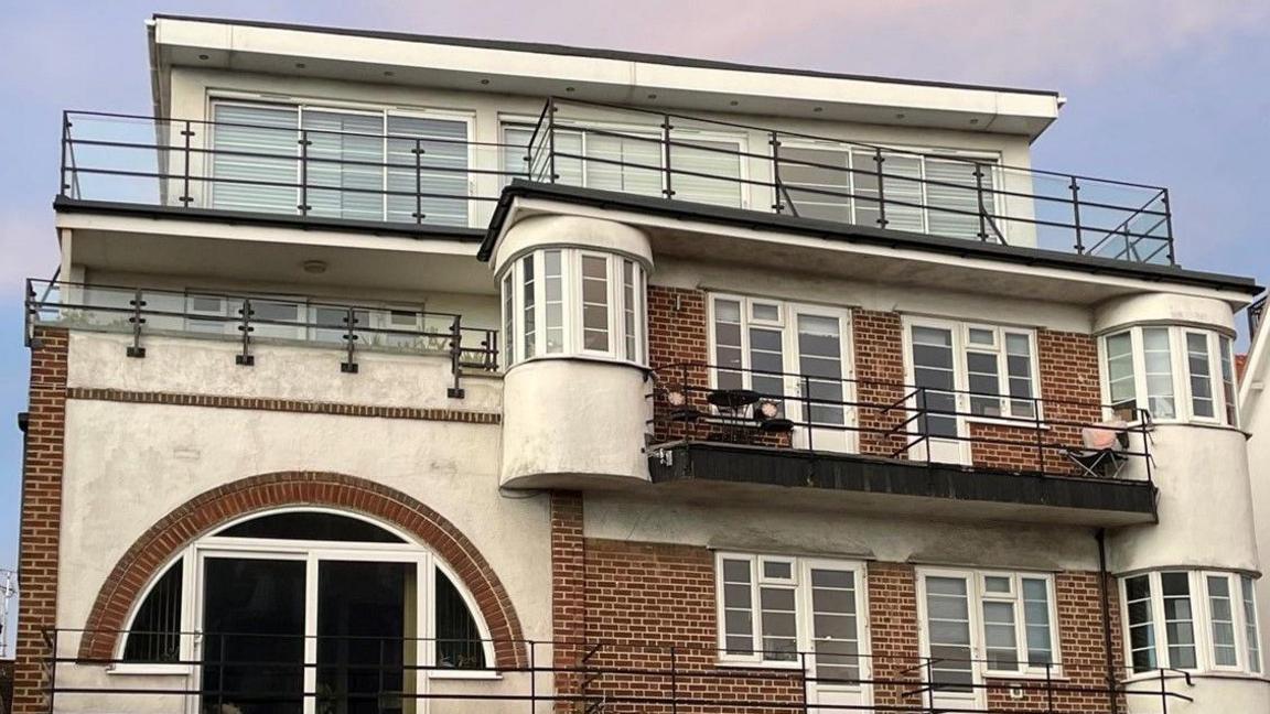 Close up of a block of art-deco flats. There are three stories with arc and rectangular windows as  well as turrets