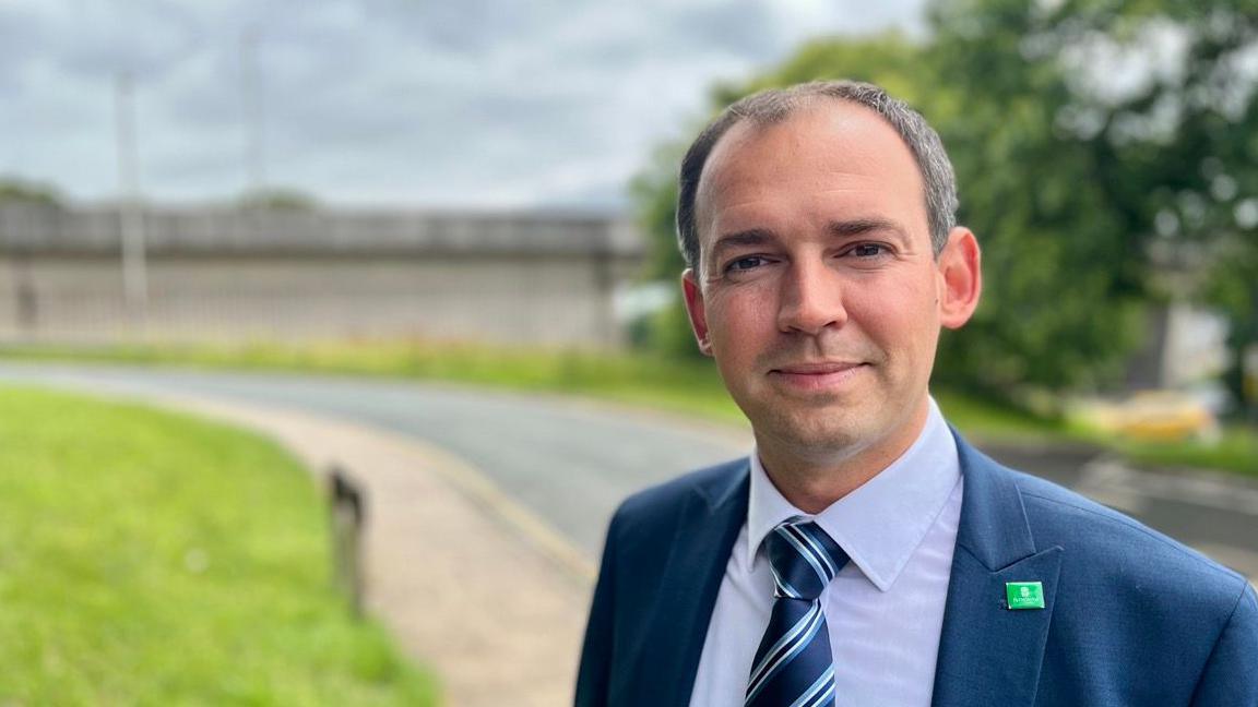 Chris Wood, Plymouth City Council member, in a blue shirt, blue striped tie and blue suit jacket with a green Plymouth City Council badge.