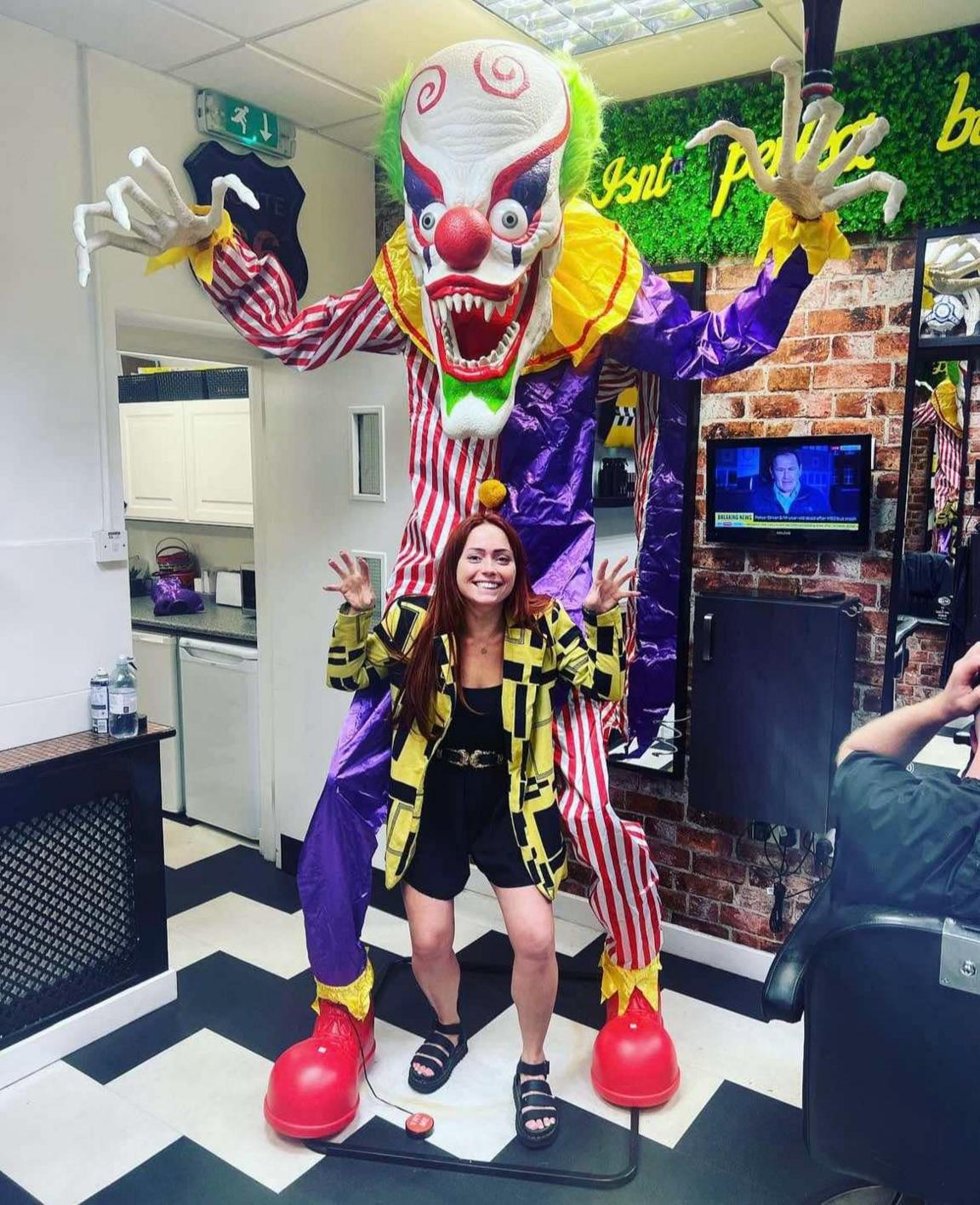 A large clown wearing yellow, purple and red patterned suit. Woman standing in front of the clown