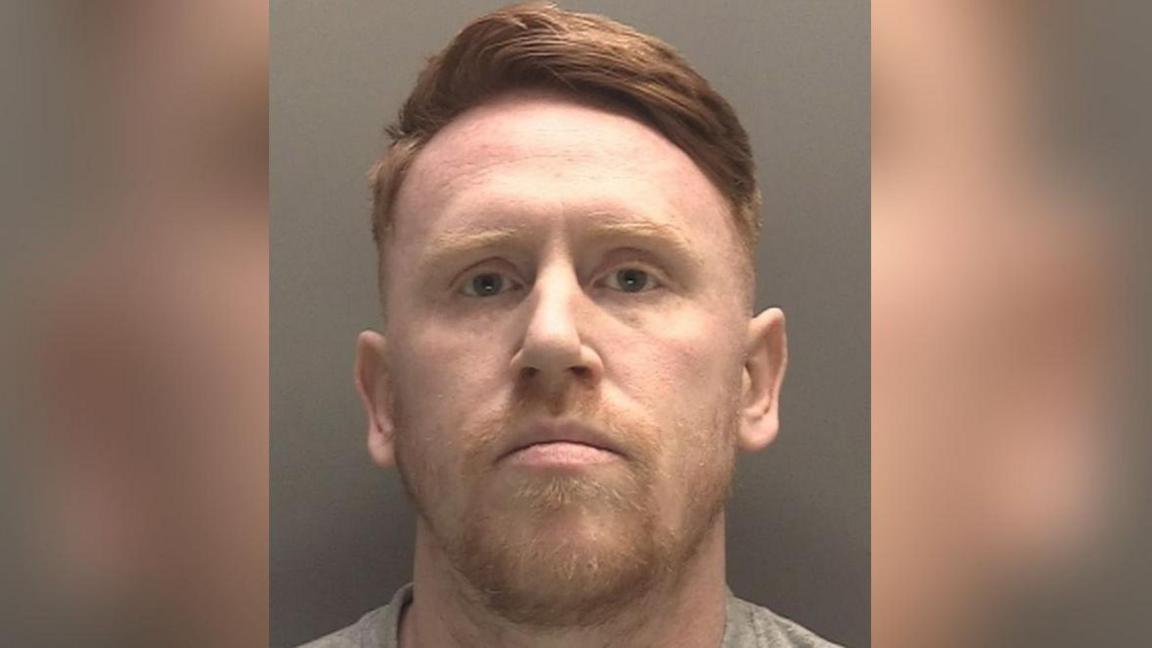 This police mugshot shows Ryan Cullen looking directly at the camera, wearing a grey top. He has a ginger beard and moustache and brown hair.