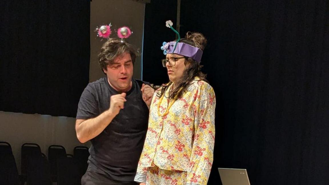 Image of Christopher and Hollie mid-scene, wearing hand-band fancy dress antennae on their heads. 