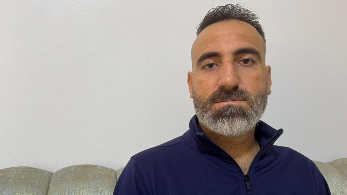 A man in his 40s with a greying beard and short dark hair looks directly at the camera