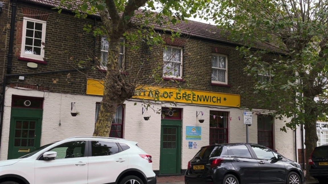 The exterior of a building "Star of Greenwich." It's a brick structure with a yellow sign above the entrance, bordered by trees on either side. Two cars are parked out front