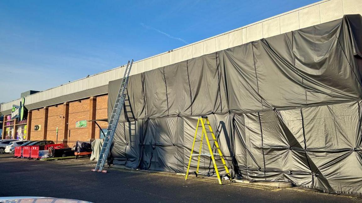 Black tarpaulin has covered the entrance to Go Bowling in Dunstable. Ladders are leaning against it. The photo is taken from the car park outside.