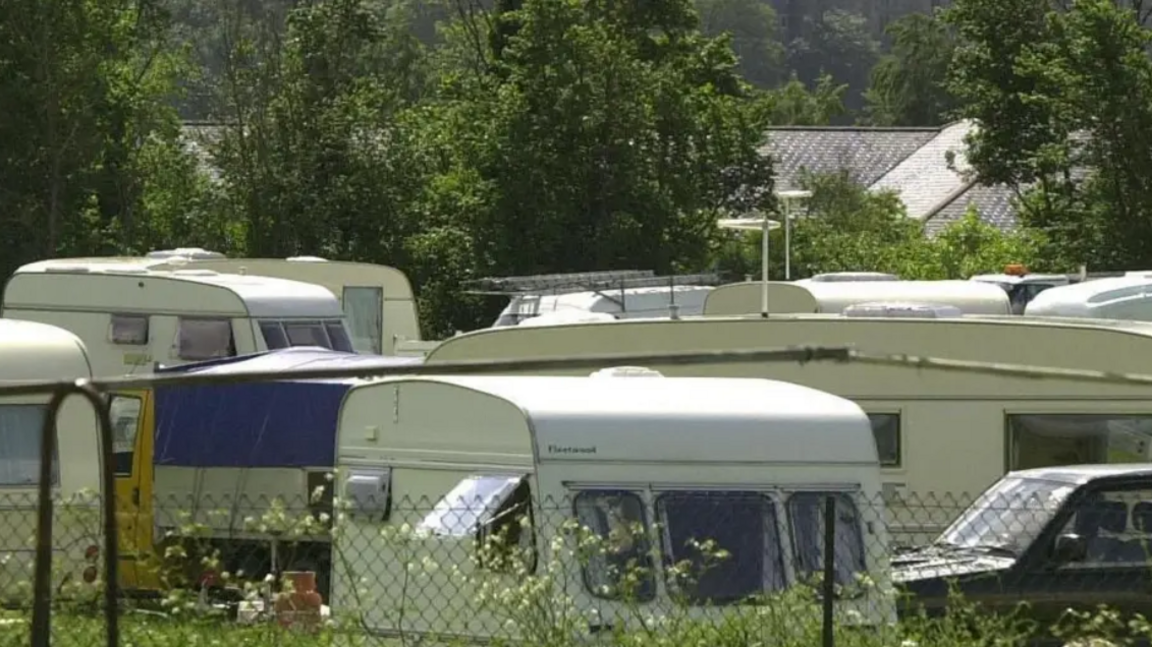White caravans stationary at a site which is behind a wire fence.