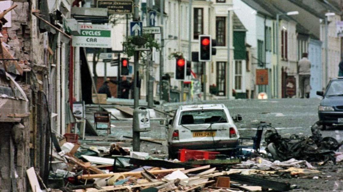 A white car parked on a street, surrounded by rubble. 