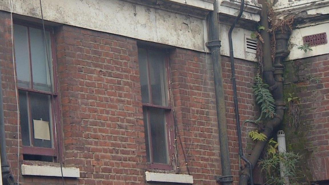 A scruffy exterior corner of the hospital with crumbling red bricks and rotten window frames