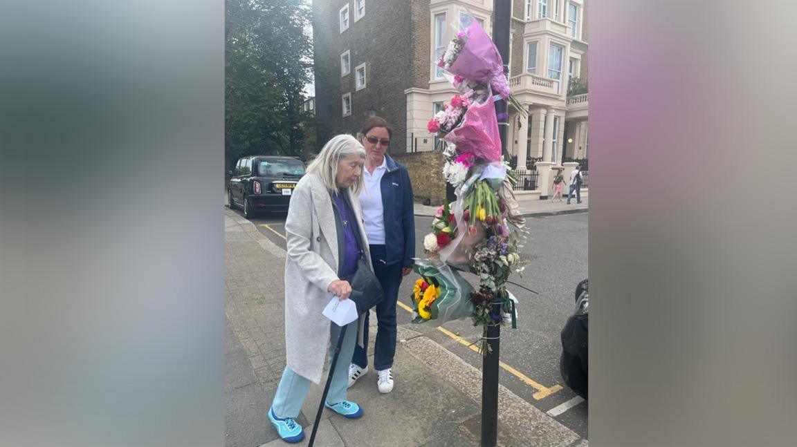 Two women stand by a lamp post covered in bunches of flowers