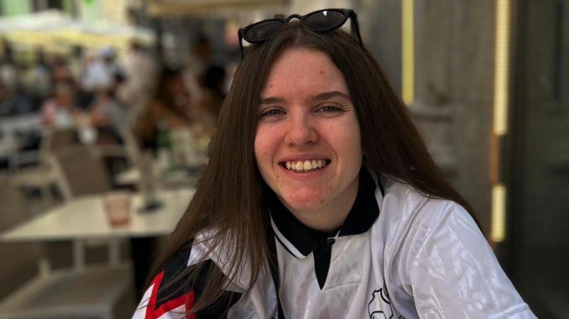 A head and shoulders shot of Amelia Warren with dark hair, sunglasses on her head and wearing a white Derby County shirt.