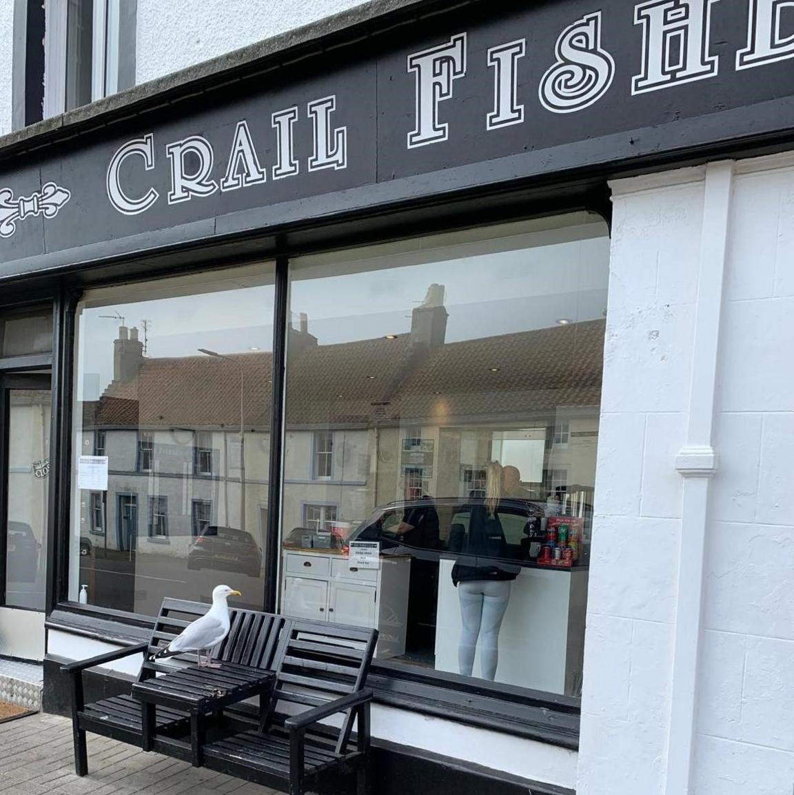 A seagull standing on a table looking into a fish and chip shop.