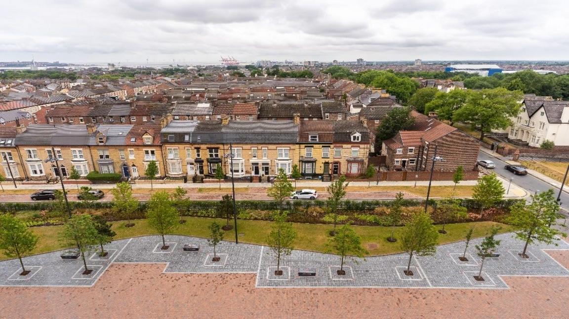 Rows of houses in front of trees in a paved area