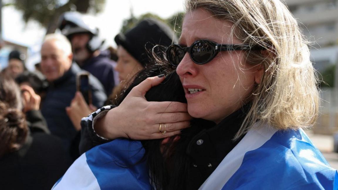 A woman draped in an Israeli flag holds another person (20/02/25)