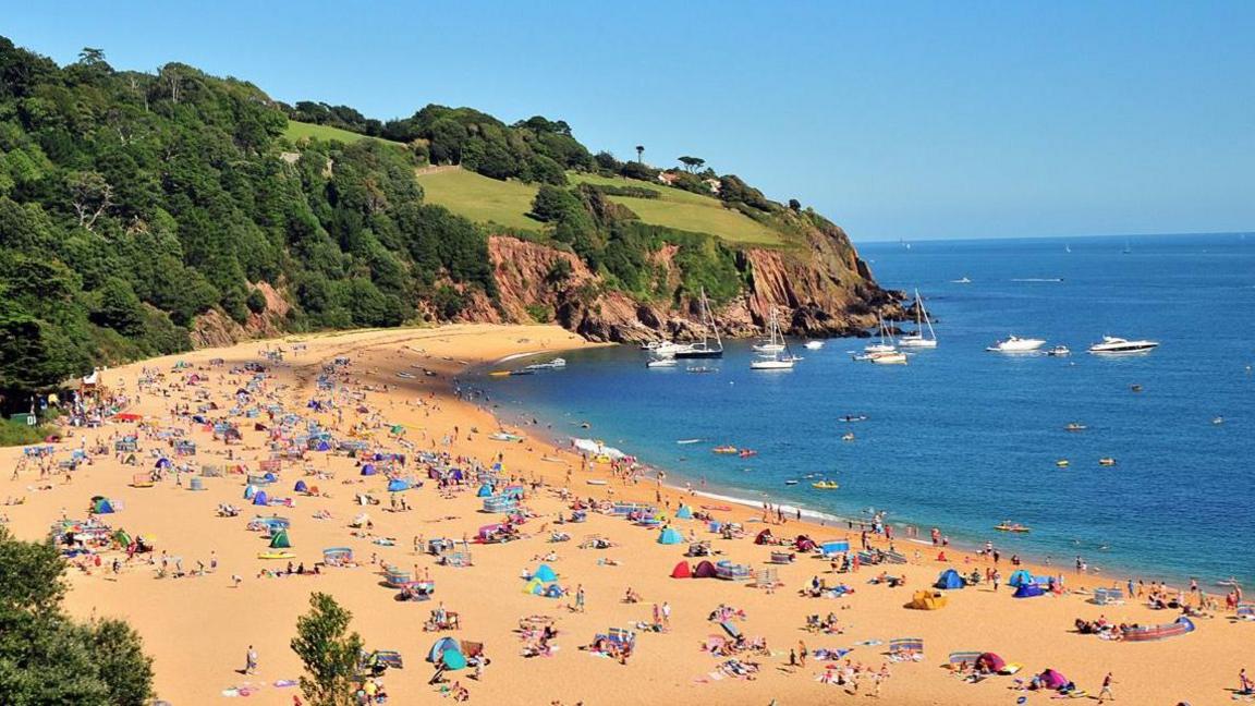 The beach at Blackpool Sands in south Devon with lots of people on the beach, some in the water and some boats moored just offshore.