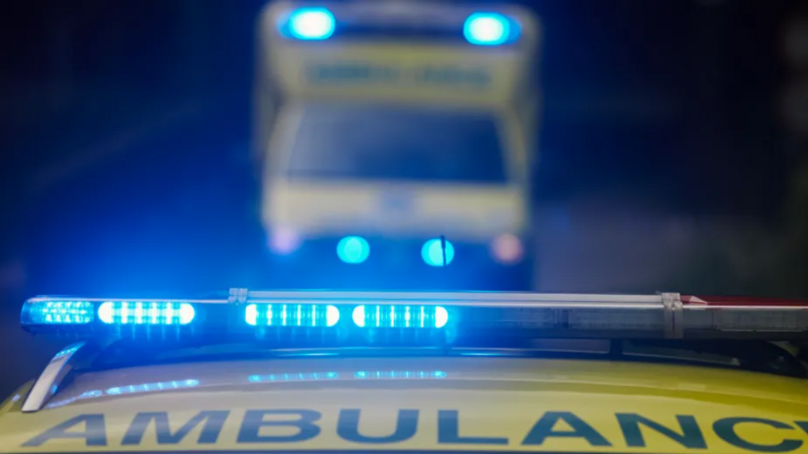 The top of an ambulance vehicle, it's lights are flashing blue and in the background an out of focus ambulance is visible