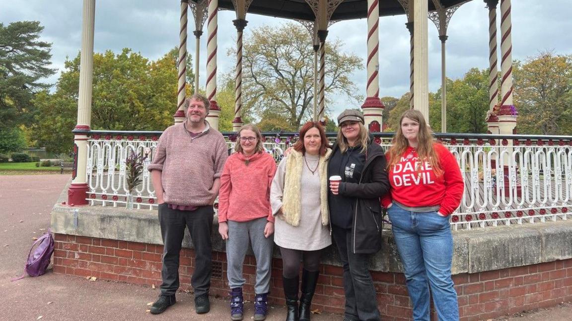 There a five people - a man and four women - are standing in a row in front of a bandstand. There are trees and greenery in the background.
The news of his death shocked the music world and millions of fans of One Direction, one of the most successful pop groups of the 2010s.