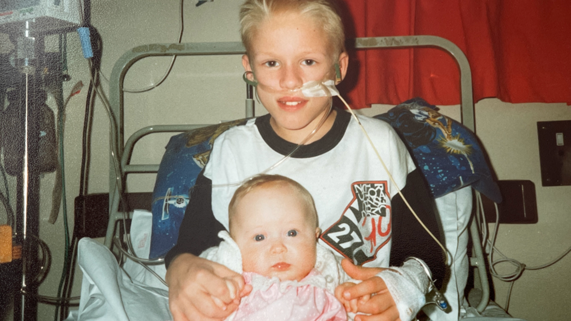 Lee sitting in a hospital bed holding his baby sister