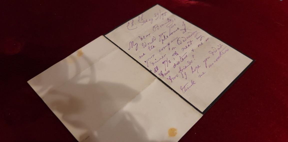 A handwritten letter on cream-coloured paper with purple ink, partially folded and placed on a red velvet surface. The letter contains cursive writing, and dates back to 1875.