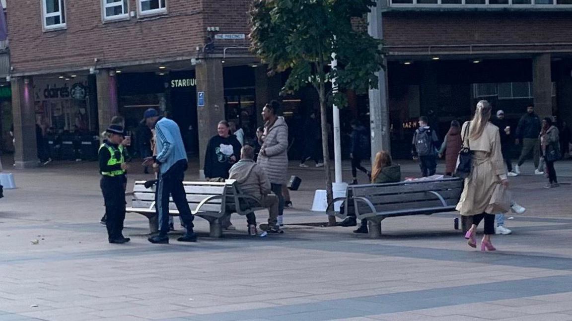 Police Community Support Officers speak to people in Broadgate, Coventry, as shoppers and other city visitors pass by