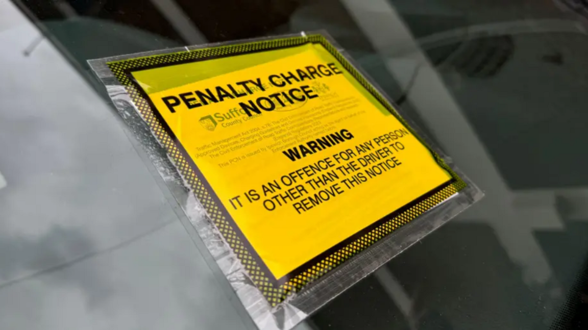 A yellow and black penalty charge notice on a car windscreen