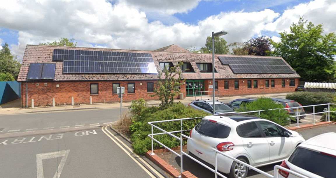 A Google Street View image of the Beccles Medical Centre - a wide brick building with solar panels on its roof