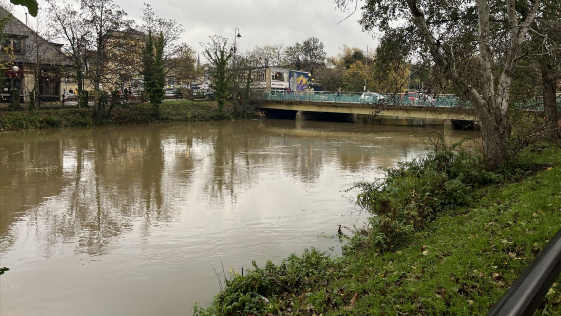 A shot of a high river in Chippenham town centre with a road and foot bridge in the background
