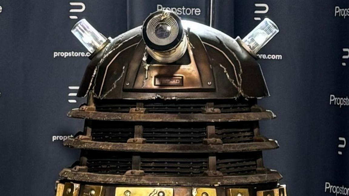 A close up of a battle-damaged Dalek with Propstore branding behind it