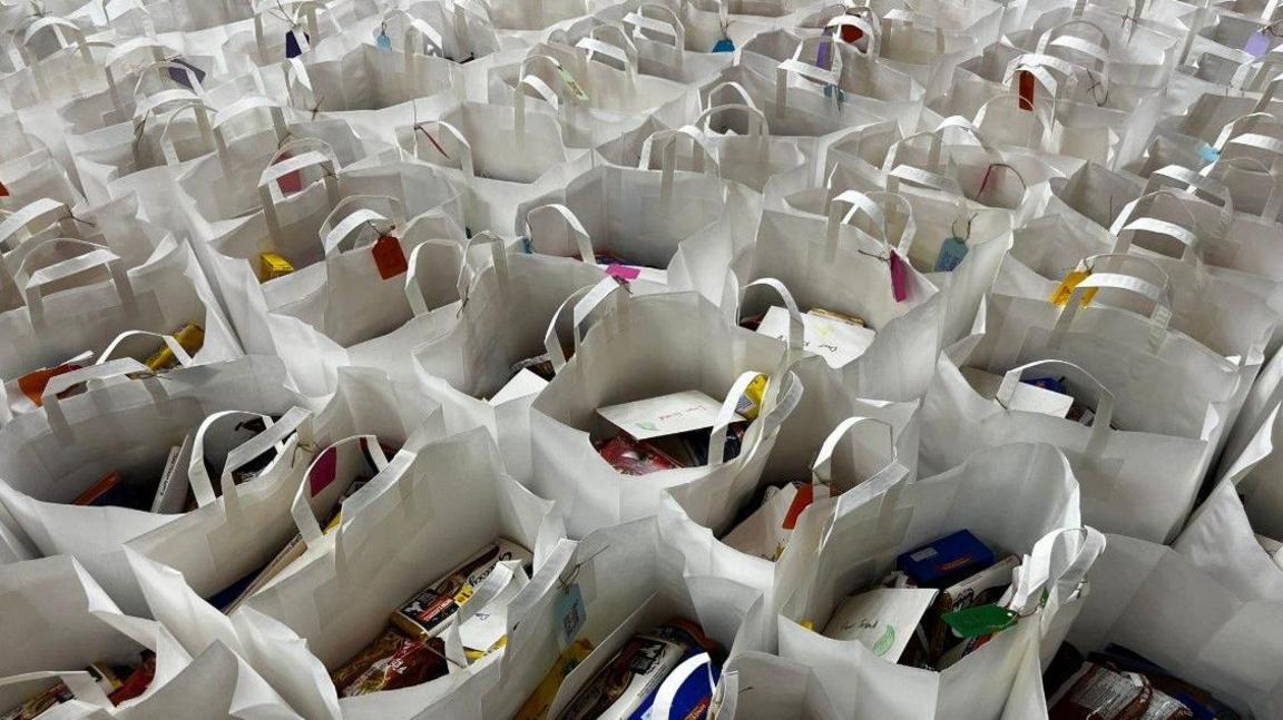 There are rows and rows of large white paper bags containing various food items.
