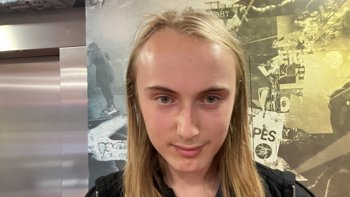Shows a teenage boy with long blond hair and wearing a black hoodie