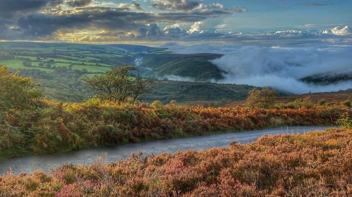 Scenery of Dunkery Beacon in Exmoor National Park - the photograph shows rolling green hills, foliage, mist and clouds in the sky 