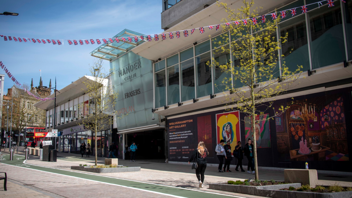 Outside view of the Mander Centre entrance in Wolverhampton showing pedestrians walking past a glass-fronted building