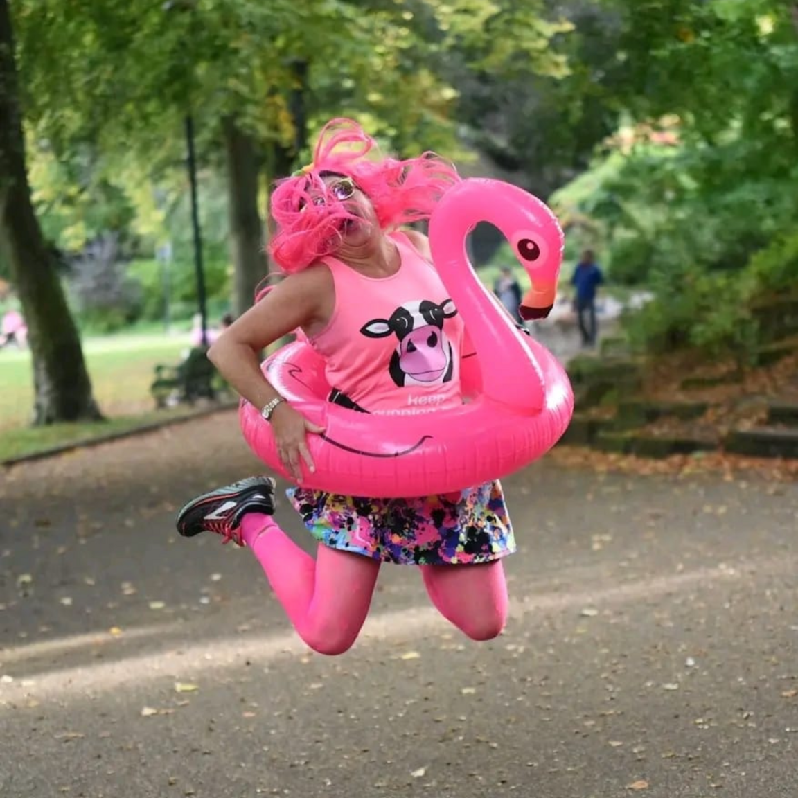 A woman jumps in the air in pink clothing, with a pink inflatable flamingo ring around her waist