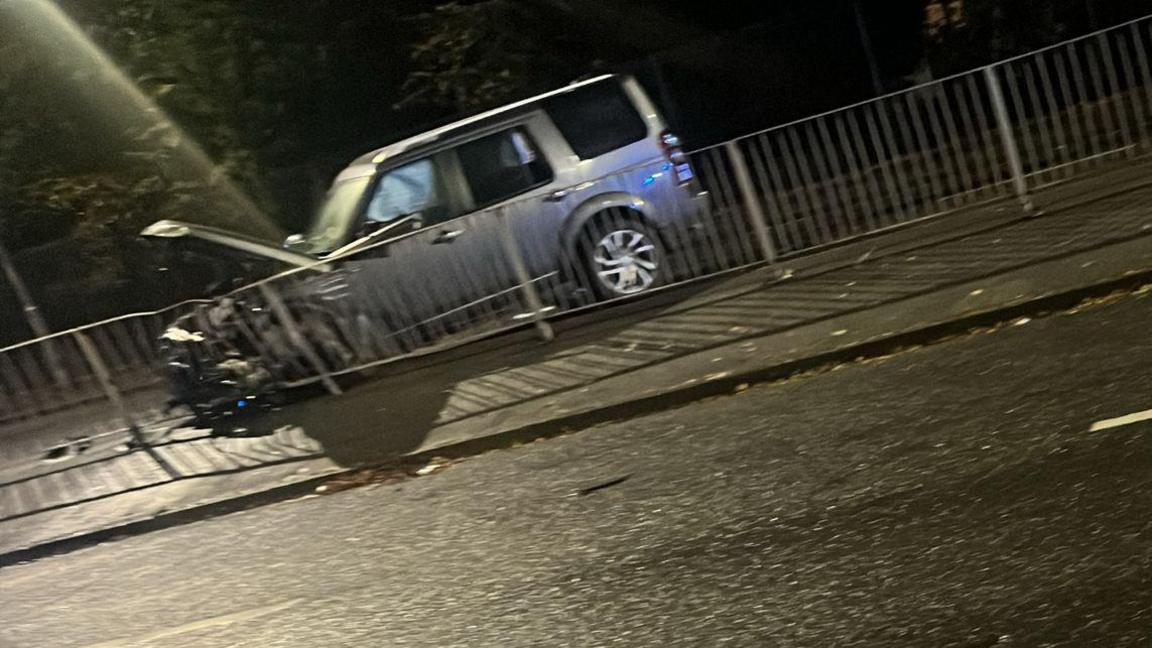 Shot of crashed silver car with its front bonnet open, on a central reservation of a dual carriageway 