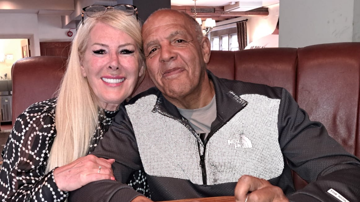 Heather - dressed in a black and white top - and Melvin - in a North Face jacket - sitting down and smiling for the camera