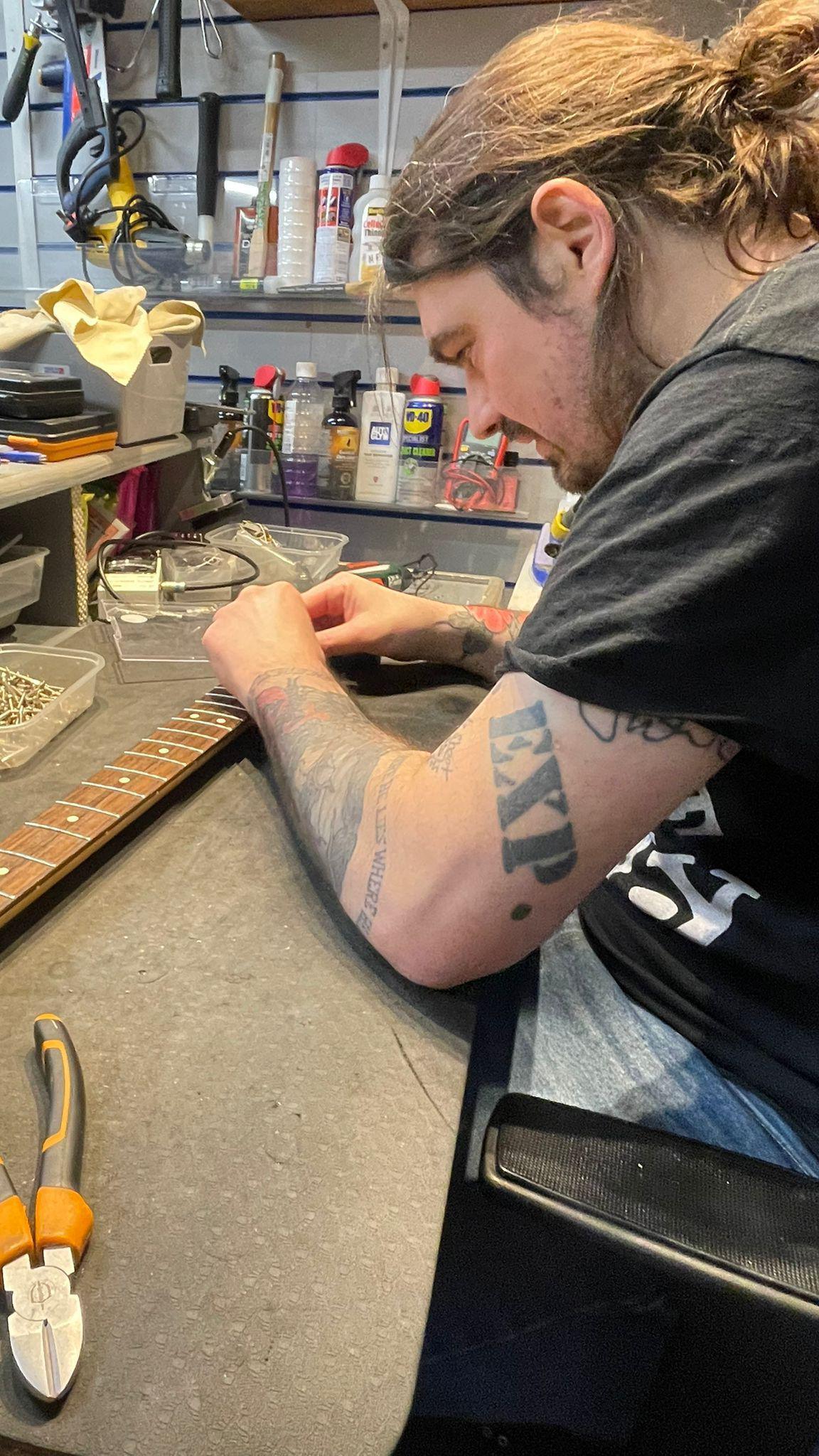 Sam Orr is working on a guitar neck, with tools around him.