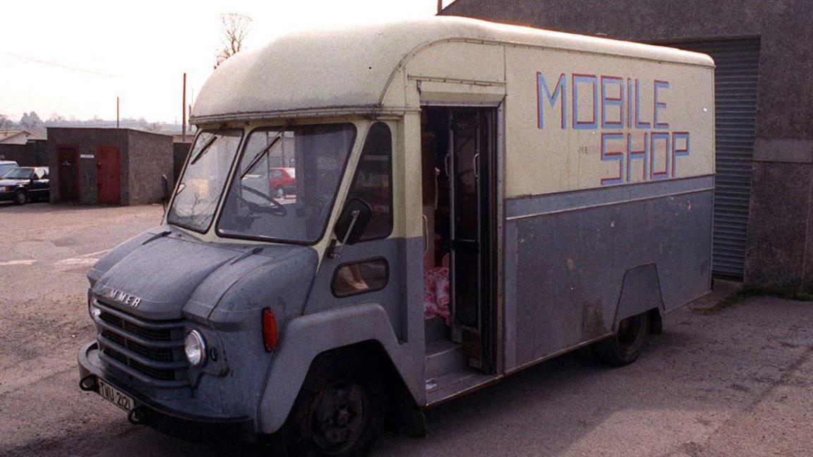 An old looking blue and white van with mobile shop on the side parked in a walled area. The van was the scene of a triple murder in 1991.