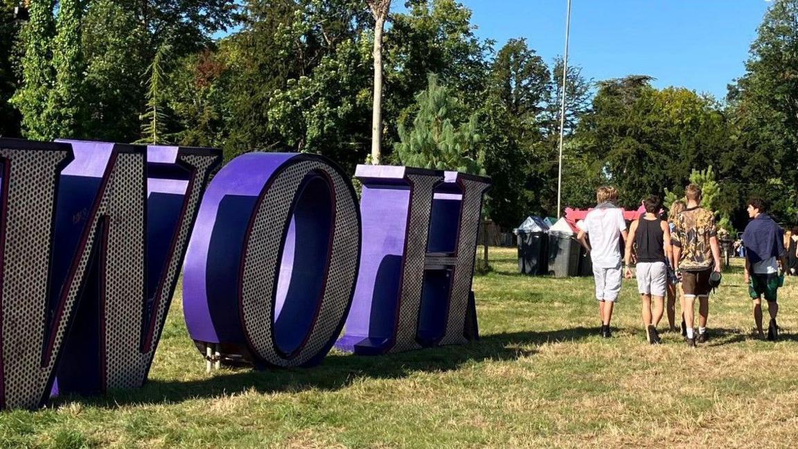 Festivalgoers walking past a large freestanding purple WOH sign