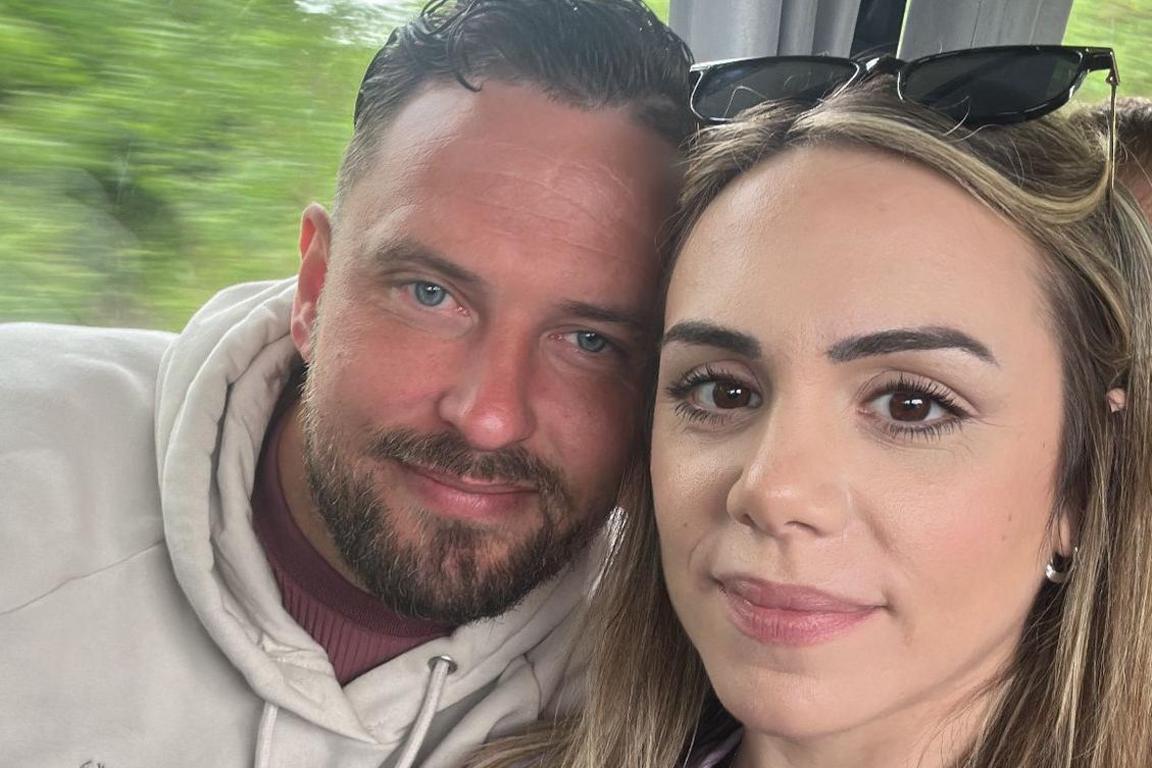 Jason and Mimi take a selfie while sat on a train, their heads touching.