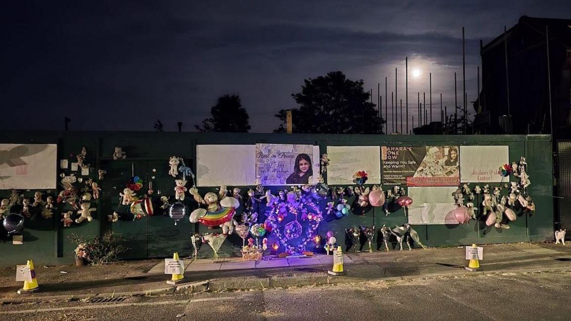 Along a road green hoardings are covered in toys, balloons and large images including photos of Sahara