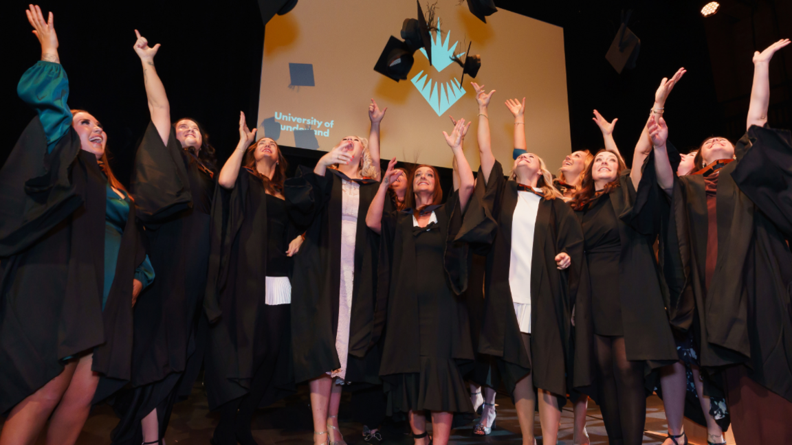 The first cohort of graduating midwives smile as they throw their caps in the air. 