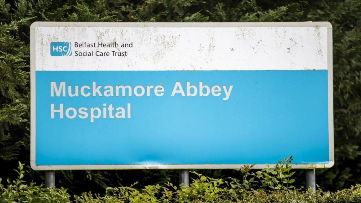 A blue sign which reads 'Belfast Health and Social Care Trust' 'Muckamore Abbey Hospital' 