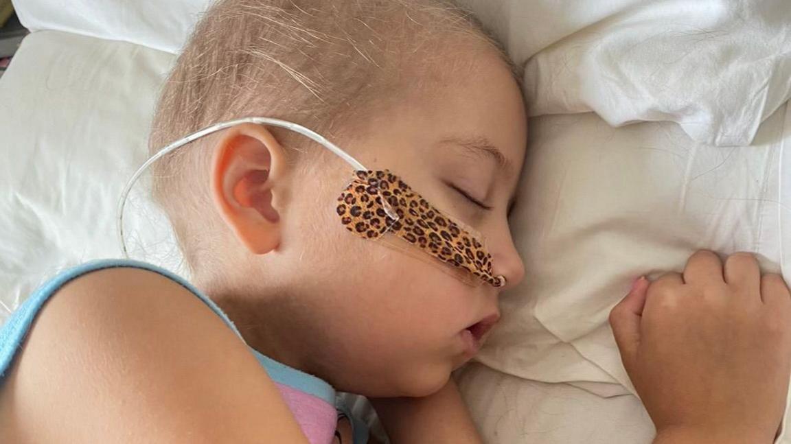 Betsy asleep on a hospital bed with a tube going up her nose and very short hair following chemotherapy. 