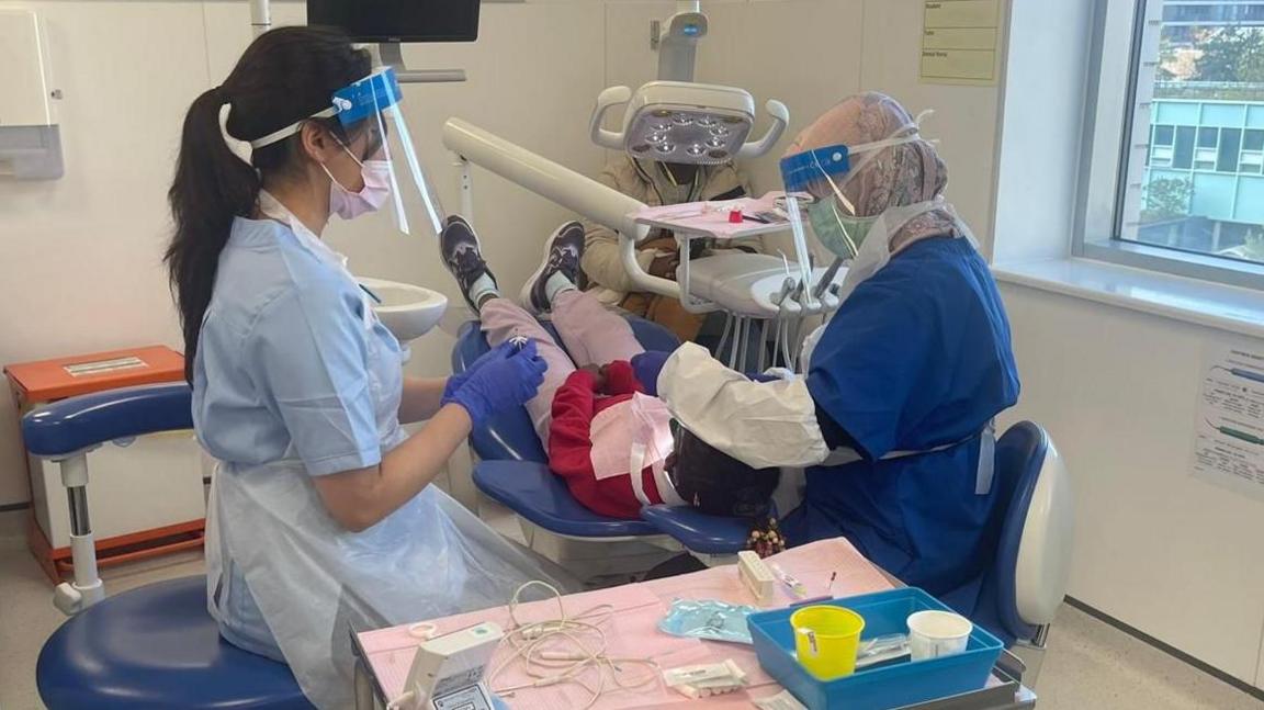 Dentists attend to a patient sitting in a dental chair
