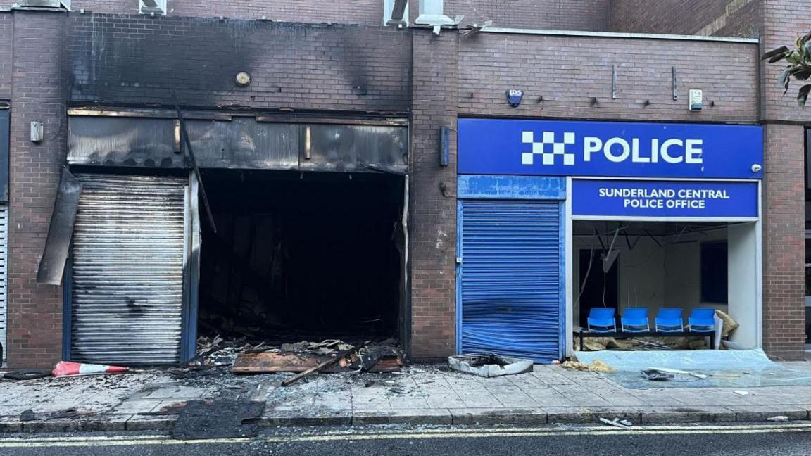 A burnt out citizens' advice office next to a small police office which has had its front window totally smashed.