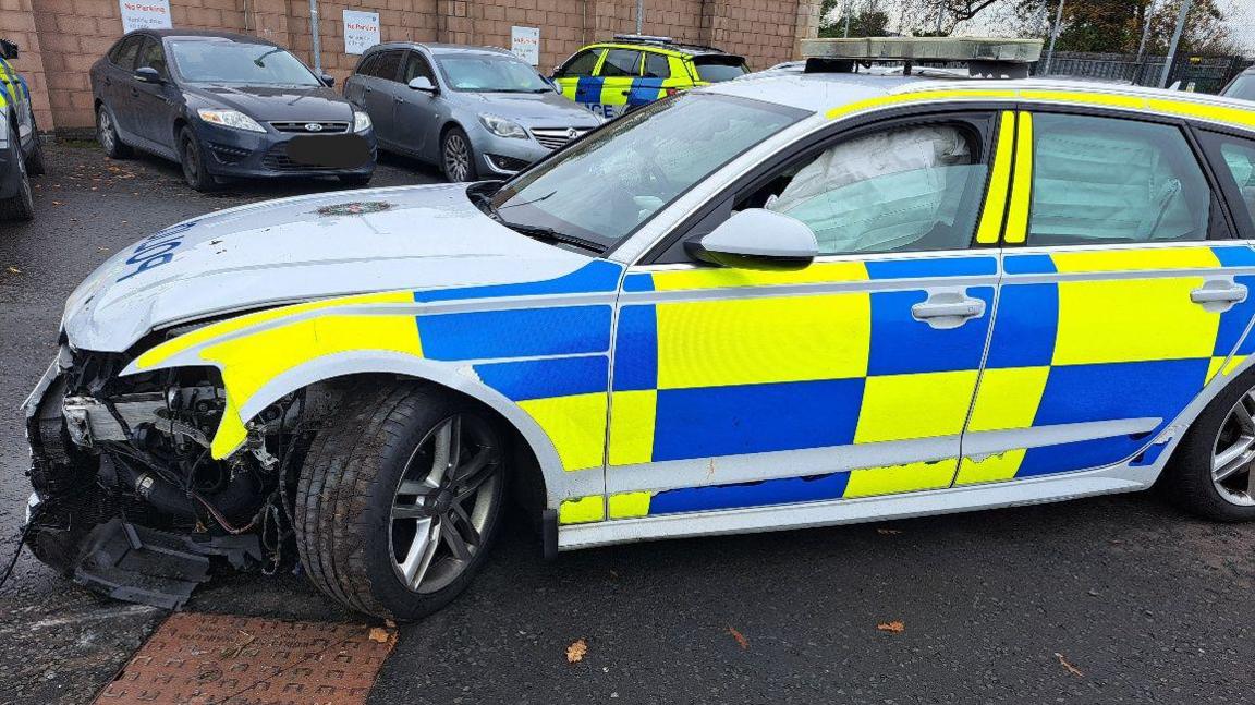 A PSNI car with damage to the front of the vehicle. The front of the car is ripped off and the is visible. 