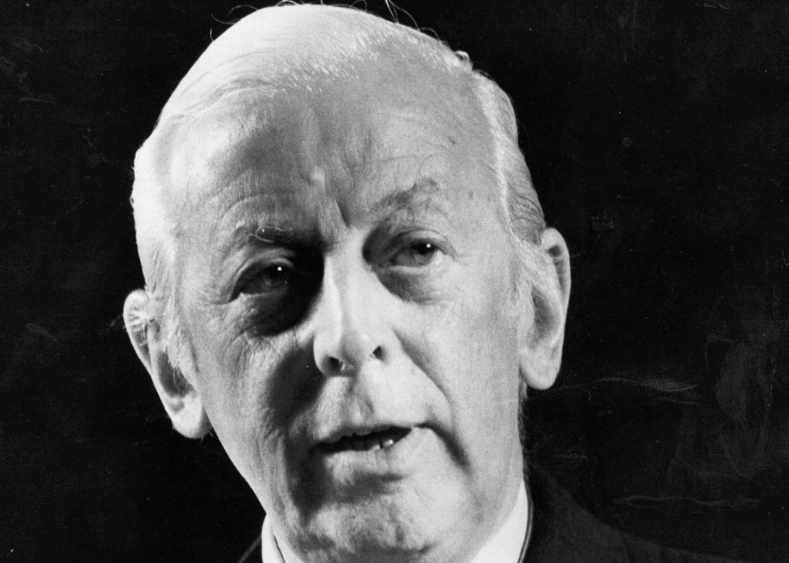 A black-and-white photo of Alistair Cooke, with his head going from the top to the bottom of the image. He is looking to the left of the camera.